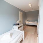 Room with two beds, wooden floor, and light walls.
