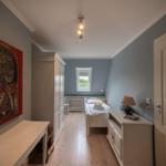 Bedroom with bed, wardrobe, and wall art. Wooden floor and window with view outside.