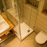 Bad mit Dusche, Waschbecken und Toilette. Holzregal und Kerzen.