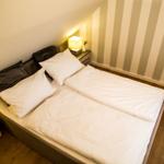 Schlafzimmer mit Doppelbett, Nachttisch und Streifenwand.