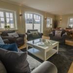 Wohnzimmer mit Sofa, Sesseln, Glas-Tisch und Holzboden.
