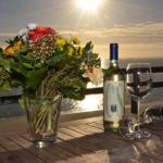 Auf der Terrasse steht ein Tisch mit Blumen, Wein und Gläsern vor Sonnenuntergang.