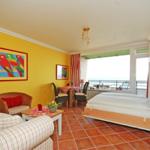 Zimmer mit Bett, Sofa, Tisch und Balkon mit Meerblick.