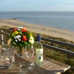 Terrasse mit Tisch, Wein und Blumen über Strand und Meer