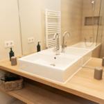 Bad mit Waschbecken, Dusche und Toilette. Holzunterlage und Spiegel.