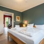 Bedroom with wooden bed, white linens, and green walls. Door leads to living area with red wall.