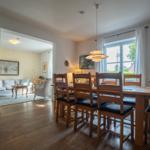 Dining room with wooden table and chairs, view into living room with sofa and rug.