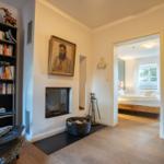 Living area with bookshelf, fireplace, and view into bedroom with bed.
