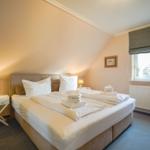 Schlafzimmer mit Doppelbett, Nachttisch und Fenster.