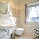 Badezimmer mit Waschbecken, Toilette und Fenster mit Vorhängen.