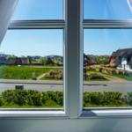 Durch das Fenster blickt man auf eine Straße mit Grünflächen und Häusern.