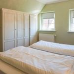 Schlafzimmer mit Doppelbett, Kleiderschrank und zwei Fenstern.