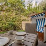 Terrace with table, chairs, and beach chair. Background: green area and fence.