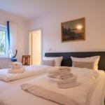 Double bed with white linens and folded towels. Window with blue curtains and nightstand with lamp.