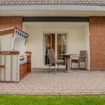 Terrace with beach chair and table with two chairs in front of house with brick wall.