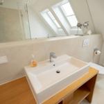 Badezimmer mit Waschbecken, Spiegel und Dusche unter Dachschrägen.