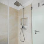 Dusche mit Duschbrause und Handbrause, beige Fliesen und Glaswand
