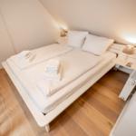 Schlafzimmer mit weißem Bett, Holzboden und Nachttisch mit Lampe.