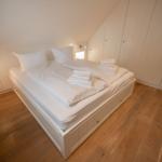 Schlafzimmer mit weißem Bett, Holzboden und Kleiderschrank.