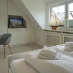 Room with double bed, TV, and window with sailboat model.