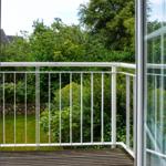 Balcony with white metal railing and view of green garden