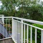 Terrace with white railing and view of green garden with flowers.