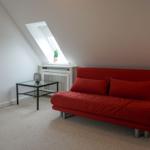 A room with red sofa, skylight, and floor lamp.