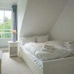 Bedroom with sloped ceiling, white bed, and window to balcony.