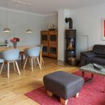 Living and dining area with wooden floor, sofa, dining table, and wood stove.