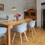 Dining room with wooden table, chairs, and wood stove. Wall art and ship model visible.