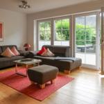 Living room with sofa, ottoman, and red rug. Entrance to terrace with garden.