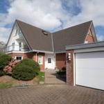 House with garage, balcony, and paved forecourt under blue sky.
