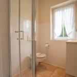 Bathroom with shower, toilet, and sink. Window with white curtains.
