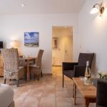 A room with sofa, table, chairs, and TV. Wall picture and tiled floor.