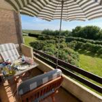 Terrace with umbrella, table and chairs. View of green garden and flowers.