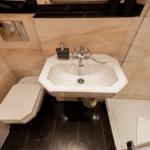 Bathroom with sink, toilet, and shower. Marble tiles and black floor.