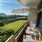 Terrace with umbrella, table and chairs. View of green lawn and flowers.