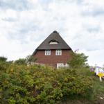 Rotes Backsteingebäude mit Strohdach und weißen Fenstern. Umgeben von grüner Vegetation und einer Treppe.