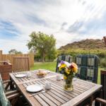 Terrasse mit Holztisch, Stühlen und Blumen. Blick auf grünen Garten und Hügel.