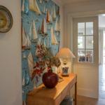 Entryway with sailboat wallpaper, wooden console, vase, and barometer.