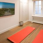 Two red yoga mats on wooden floor, wall-mounted TV, and window with radiator.