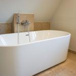 Freestanding bathtub with showerhead in bathroom with stone wall