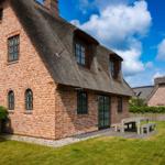 Red brick building with thatched roof and wooden terrace in the garden.