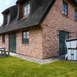 Red brick house with thatched roof, garden with table and lounge chairs.