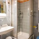 Badezimmer mit Dusche, Waschbecken und Toilette. Fliesenwand und Spiegel sichtbar.