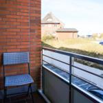 Balkon mit Stuhl und Tisch, Blick auf Haus und Grünfläche.