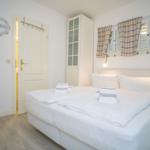 Schlafzimmer mit weißem Bett, Gardinen und Schrank. Tür führt in Bad.