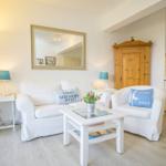 Wohnzimmer mit Sofa, Sessel und Küchenbereich. Holzfußboden und Spiegel an der Wand.