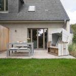 Terrasse mit Tisch, Bänken und Liegestuhl. Hinterhof mit Rasen und Hecke.