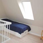 A bedroom with sloped ceiling, bed, crib, and window.